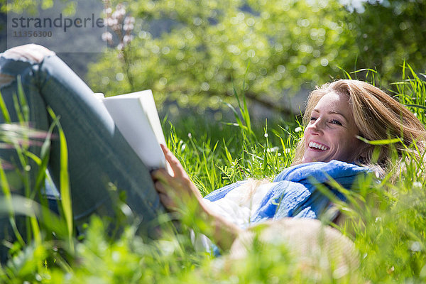 Frau liegt im Gras und liest