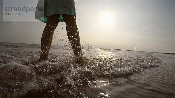 Beine einer Frau an der Küste beim Spaziergang im Meer