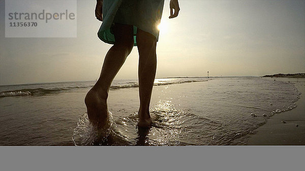 Beine einer Frau an der Küste beim Spaziergang im Meer