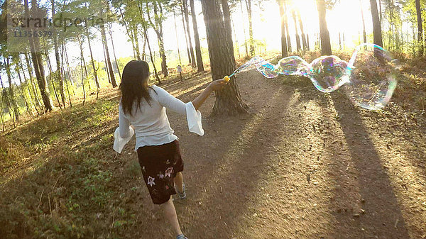 Rückansicht einer Frau im Wald  die mit einem Blasenzauberstab läuft