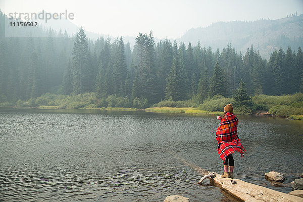 In Schottenkaro-Decke gehüllte Frau trinkt Kaffee am nebligen See  Mount Hood National Forest  Oregon  USA