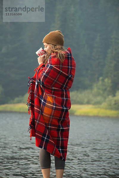 In Schottenkaro-Decke gehüllte Frau trinkt Kaffee am See  Mount Hood National Forest  Oregon  USA