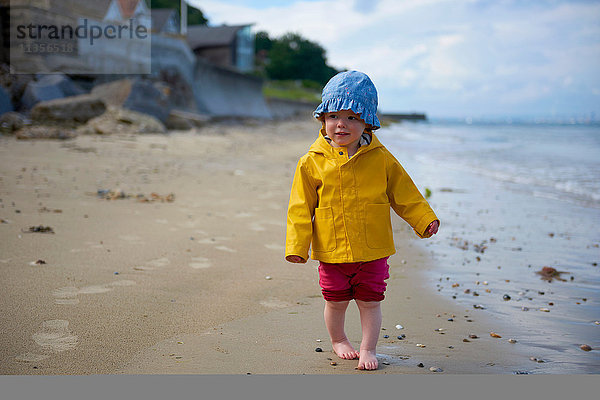 Kleines Mädchen am Strand mit Sonnenhut und Regenmantel