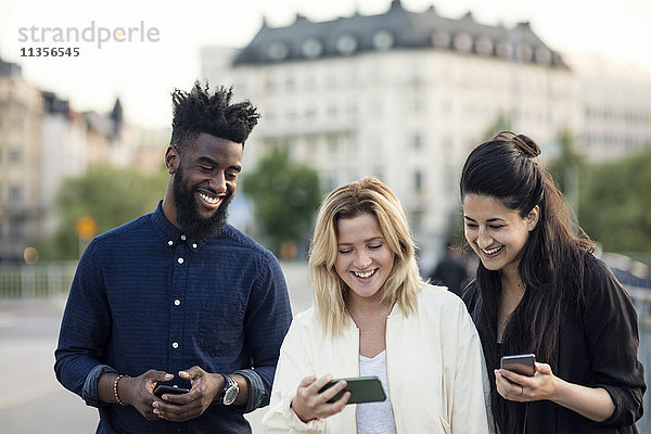 Glückliche Freunde schauen sich das Handy in der Stadt an