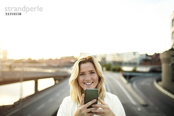Porträt einer glücklichen Frau mit Handy gegen den Himmel