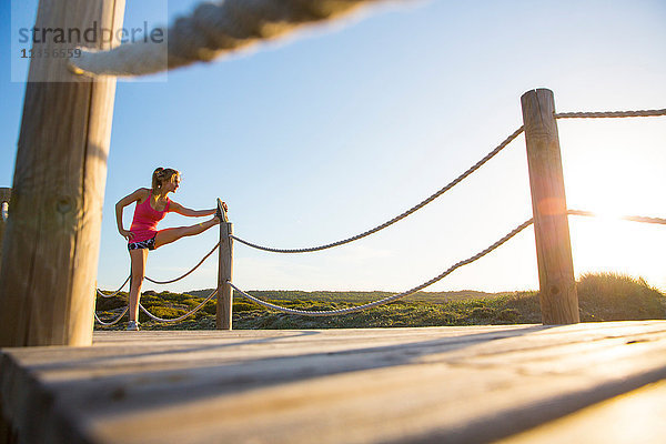 Junge Frau auf Holzbahn  Sport treiben  Bein strecken  niedriger Blickwinkel