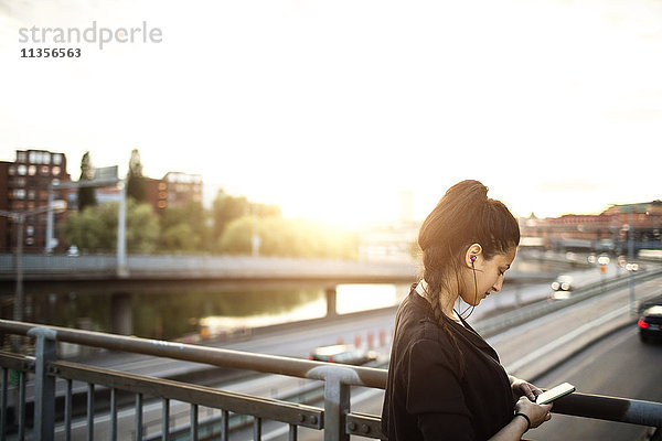 Seitenansicht der Frau mit dem Handy auf der Stehbrücke gegen den Himmel