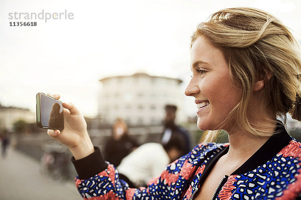 Seitenansicht der glücklichen Frau beim Fotografieren vom Smartphone aus