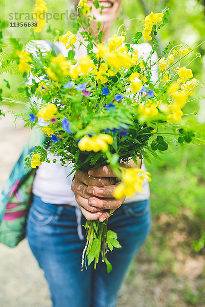 Schnappschuss einer Frau  die einen Strauss frischer gelber Wildblumen im Garten hält