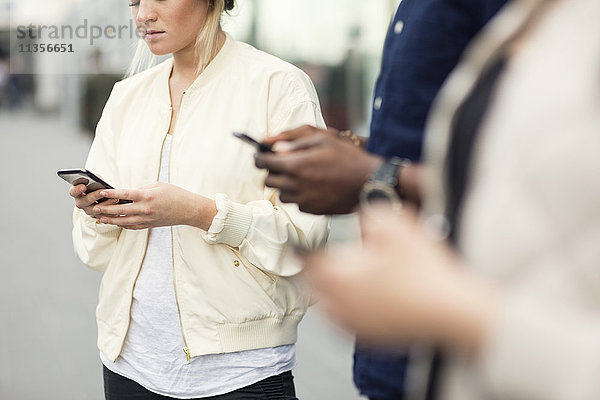 Mittelteil der jungen Freunde mit Smartphones in der Stadt