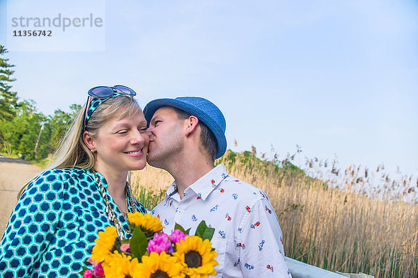 Paar hält Blumen und küsst sich auf die Wange