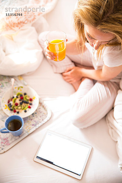 Draufsicht einer jungen Frau am Bett beim Lesen des digitalen Tabletts am Morgen