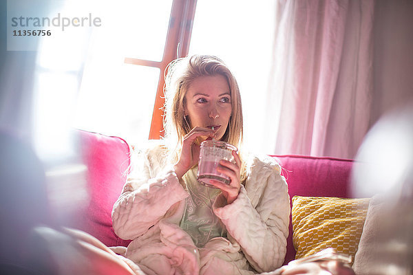 Junge Frau entspannt sich auf dem Sofa und trinkt Smoothie