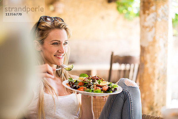 Junge Frau entspannt sich auf der Gartenterrasse und isst Salat