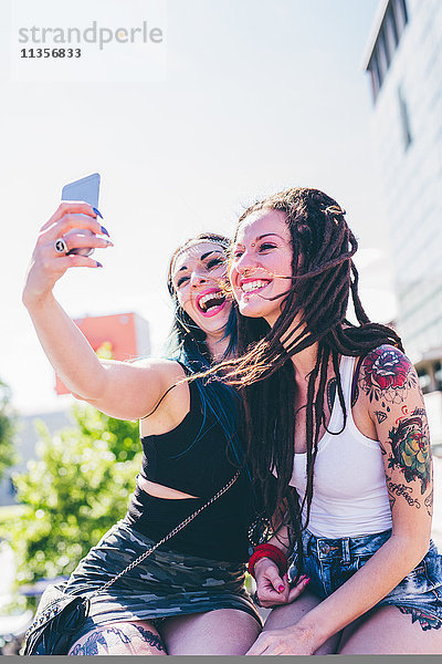 Zwei junge Frauen an der Wand nehmen Smartphone Selfie in städtischen Wohnsiedlung