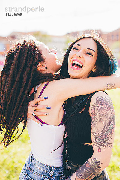 Tätowierte junge Frauen lachend und umarmend im Stadtpark