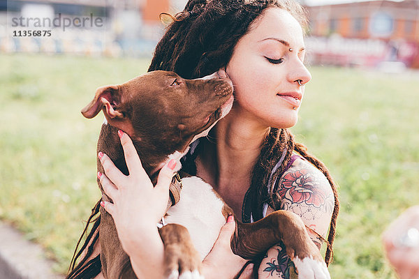 Pit Bull Terrier leckt tätowierte junge Frau im Stadtpark