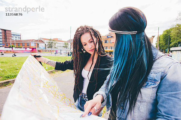 Zwei junge Frauen mit Dreadlocks und gefärbten Haaren  die auf die Karte im Stadtpark zeigen.