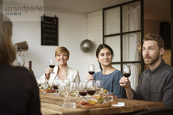Lächelnde Geschäftsleute sitzen am Tisch und halten Weinglas.