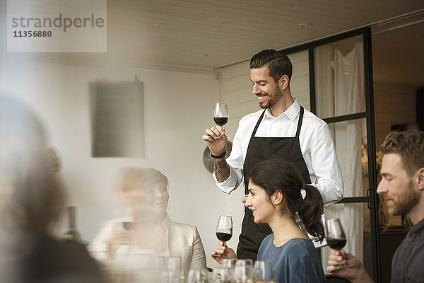 Lächelnde Menschen mit Weinglas beim Diskutieren am Tisch