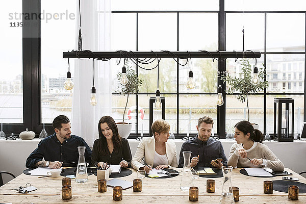 Geschäftsleute diskutieren am geschmückten Tisch gegen Fenster im Büro