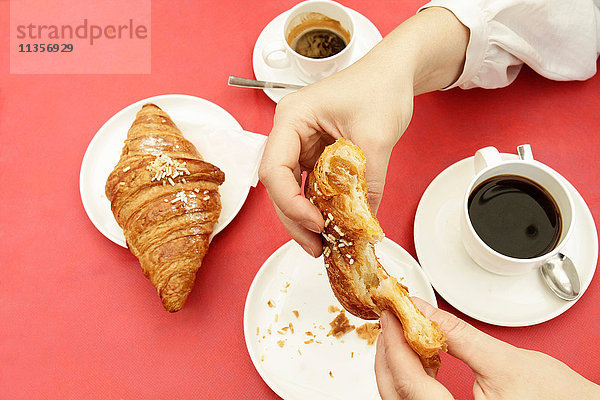 Nahaufnahme der Hände einer Frau  die im Strassencafé ein Croissant zerbricht