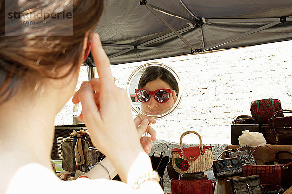 Spiegelbild einer Frau beim Anprobieren einer Sonnenbrille am Marktstand  Mailand  Italien