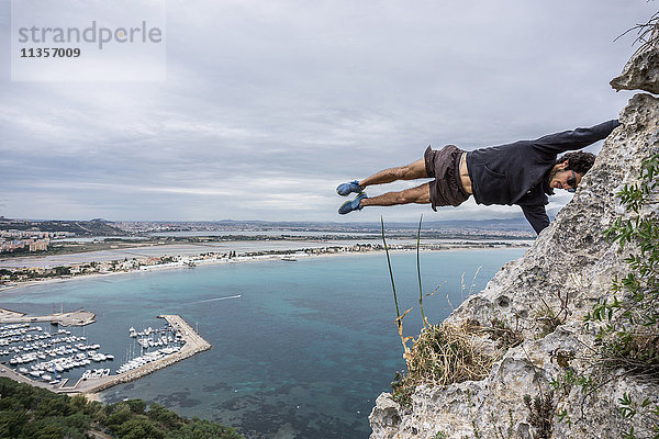 Männlicher Bergsteiger balanciert horizontal mitten in der Luft auf einem Küstenfelsen  Cagliari  Italien