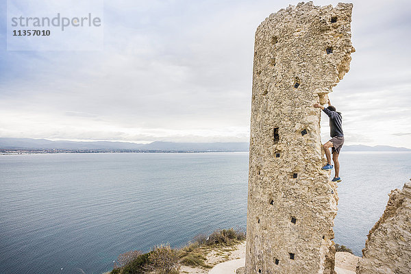 Männlicher Bergsteiger klettert Turmruine an der Küste  Cagliari  Italien