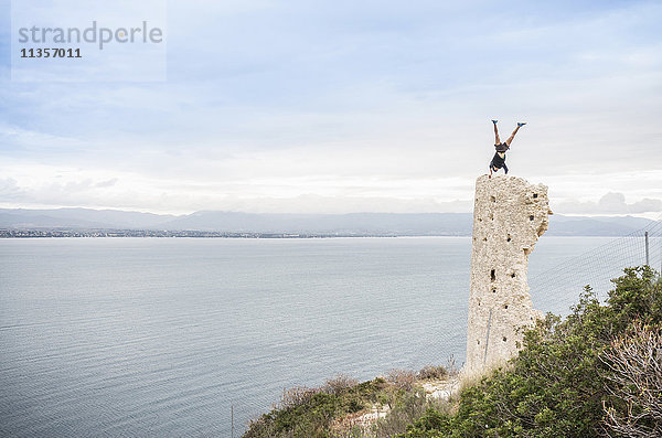 Männlicher Bergsteiger im Handstand auf der Spitze einer Turmruine an der Küste  Cagliari  Italien