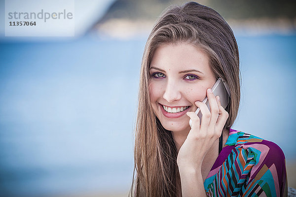 Hübsche junge Frau spricht am Strand mit einem Smartphone  Costa Rei  Sardinien  Italien