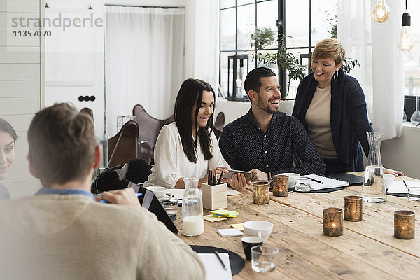 Fröhliche Geschäftsleute diskutieren am gedeckten Tisch während der Besprechung im Büro