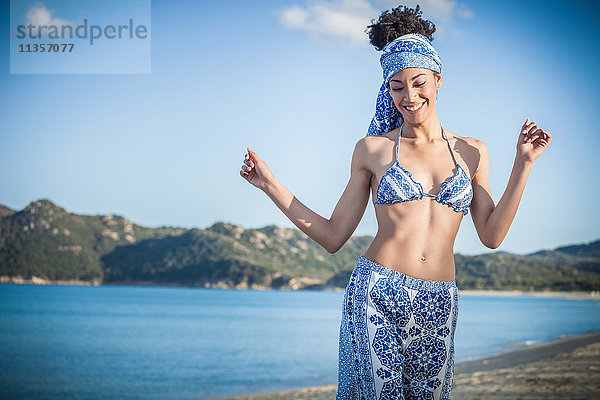 Hübsche junge Frau in Bikini-Oberteil und Sarong tanzend am Strand  Costa Rei  Sardinien  Italien