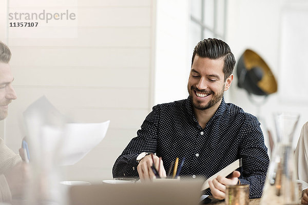 Fröhlicher Geschäftsmann beim Lesen von Dokumenten am Tisch im Büro