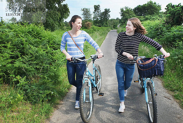 Zwei junge Erwachsene schieben Fahrräder und unterhalten sich auf dem Feldweg
