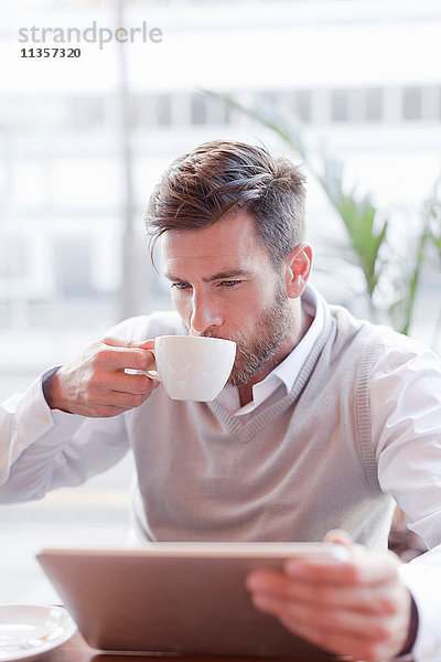 Reifer Mann sitzt im Café  trinkt Kaffee und benutzt ein digitales Tablett