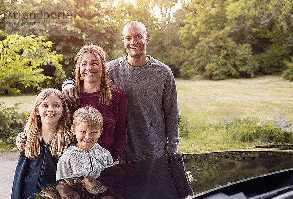 Porträt der glücklichen Familie am schwarzen Elektroauto im Park