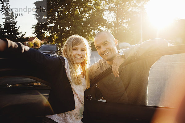 Porträt eines glücklichen Vaters und einer glücklichen Tochter  die an einem sonnigen Tag im Auto stehen.