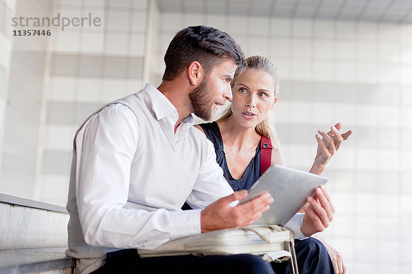 Reifer Mann und Frau sitzen auf Stufen und schauen auf ein digitales Tablett