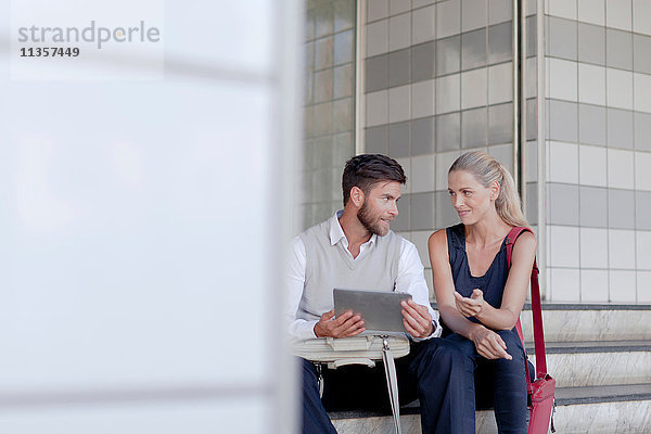 Reifer Mann und Frau sitzen im Freien und schauen auf ein digitales Tablet
