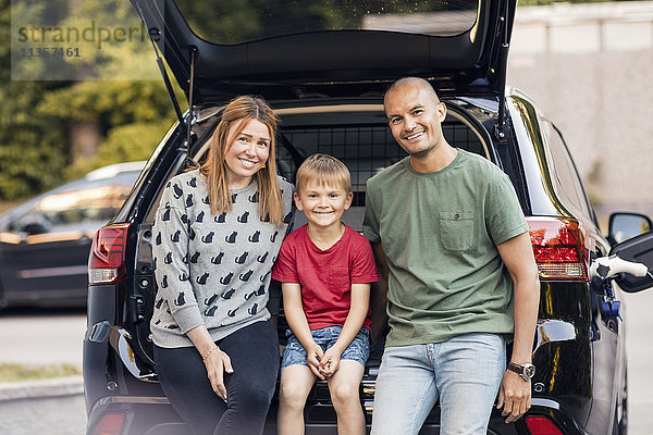 Porträt einer glücklichen Familie  die im Kofferraum im Hinterhof sitzt.