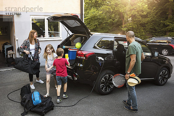 Familie mit Gepäck und schwarzem Elektroauto im Hinterhof