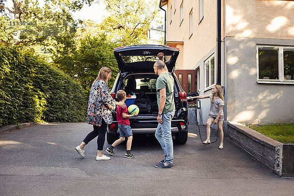 Familie steht bei Elektroauto mit offenem Kofferraum im Hinterhof