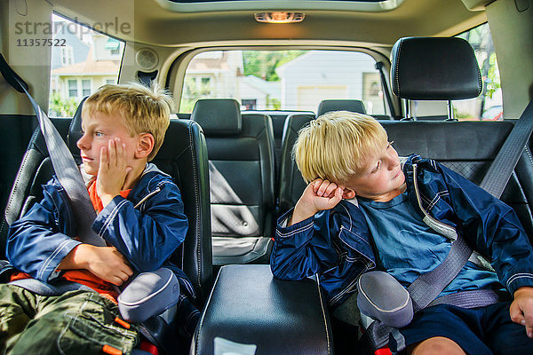 Zwillingsbrüder sitzen hinten im Fahrzeug  gelangweilte Mienen