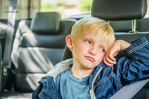 Junge Junge sitzt hinten im Fahrzeug  gelangweilter Gesichtsausdruck