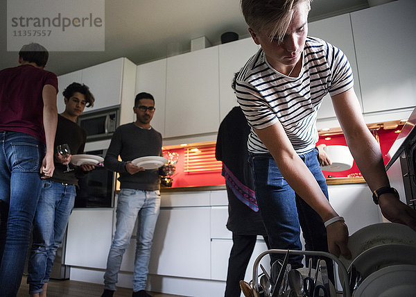 Blick auf den Teenager  der nach dem Abendessen Teller in der Geschirrspülmaschine anordnet.