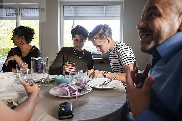 Freunde  die telefonieren  während die Familie am Esstisch in der Dinnerparty redet