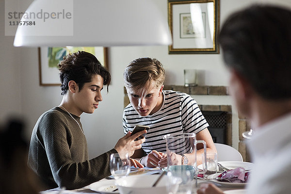 Freund zeigt dem Teenager das Telefon  während er auf der Dinnerparty sitzt.