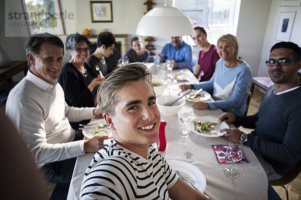 Blick auf den lächelnden Teenager  der sich mit seiner Familie und Freunden am Esstisch vergnügt.