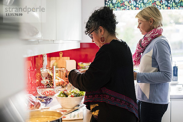 Multiethnische Freunde bereiten Salat in der Küche zu Hause zu.